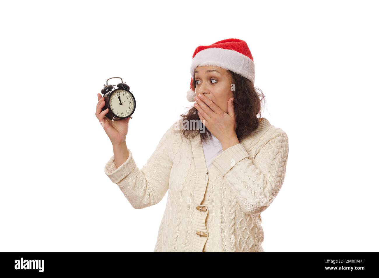 Surprised woman expresses astonishment stupefaction, looking at retro black alarm clock showing midnight. Happy New Year Stock Photo