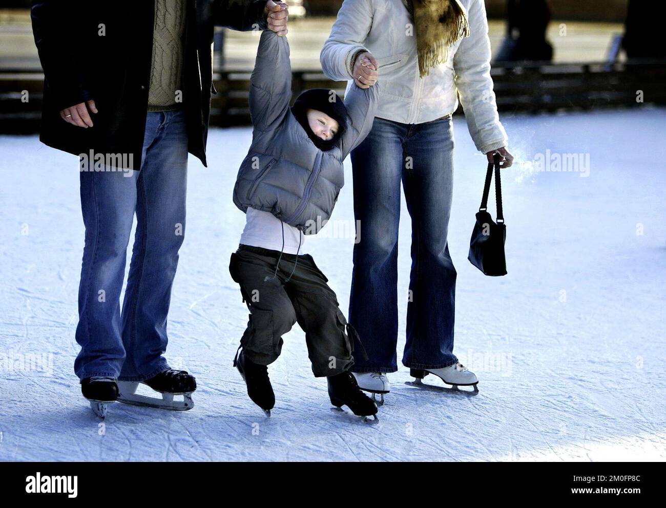 The ice skating rinks are open in Copenhagen. This little boy is out trying on his skates for the first time this season. It is not as easy at it looks. His mum and dad try to keep him upright. 'Frederiksberg Have' is a beautiful garden in the summer, and a popular playground for children all year around. Stock Photo