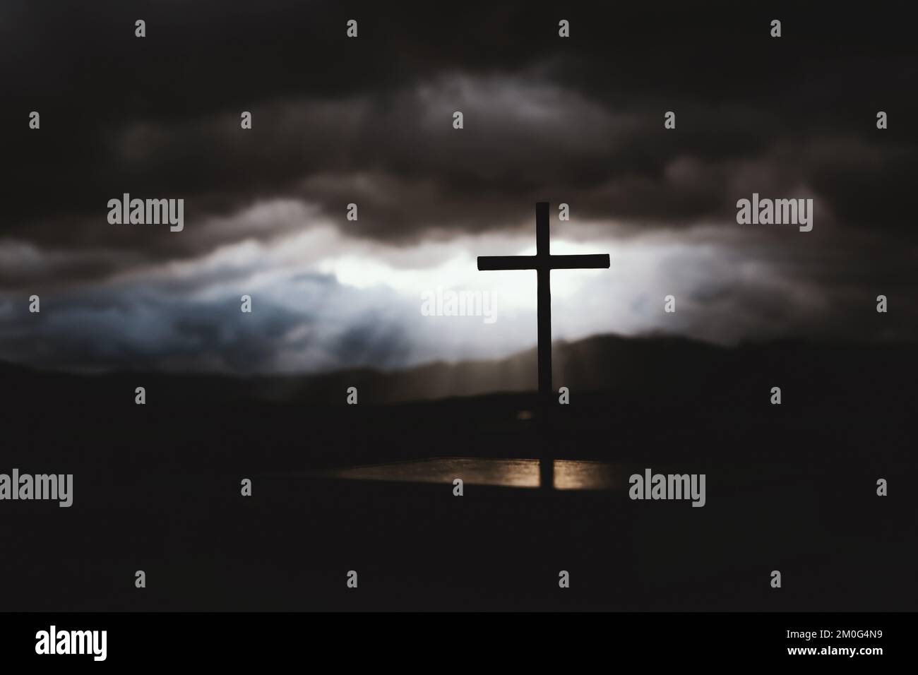A beam of light shining through a bright sky and flowing clouds, and a silhouette of the holy cross symbolizing the suffering, death, and resurrection Stock Photo