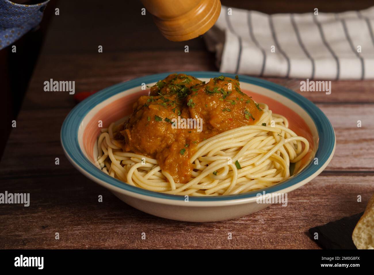 close-up of a plate of meatballs with spaghetti and parsley, pouring pepper, on a wooden table Stock Photo