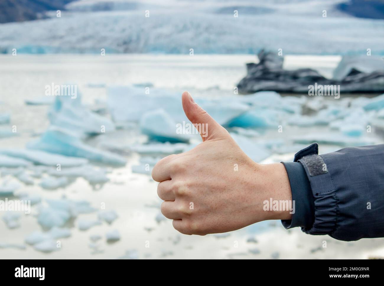 Person hand showing thumb up emotion towards climate change and global warming, climate change averted concept. Blue glacier on background. Stock Photo