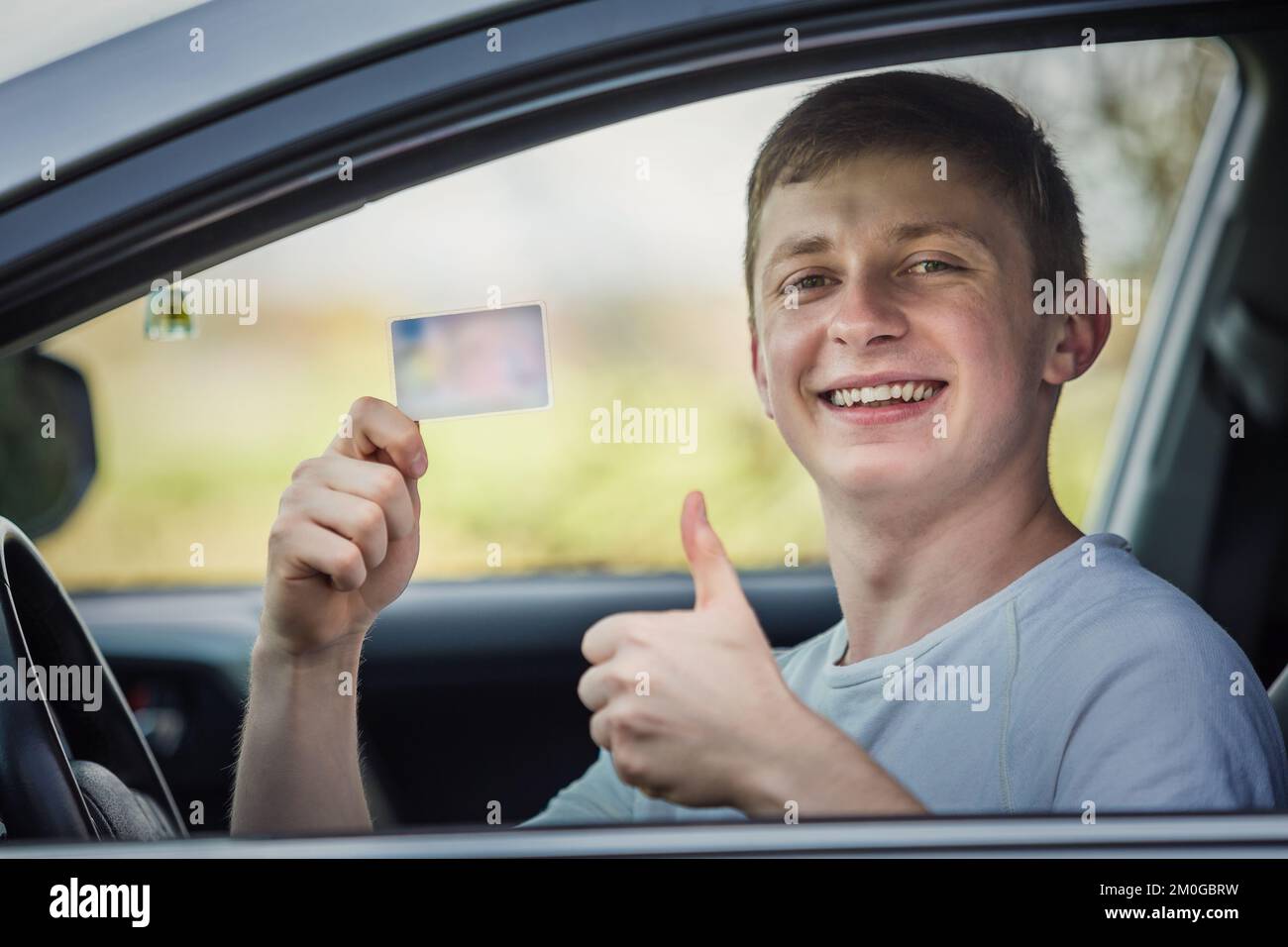 Happy and proud guy showing his driver license out of the car window while keeps thumb up gesture Stock Photo