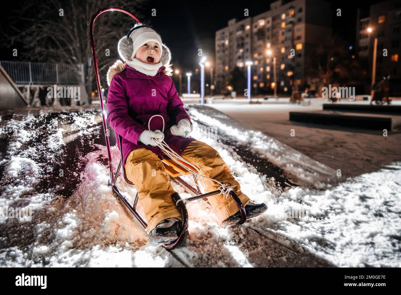 A little girl is sledding on a snowy winter evening. Stock Photo