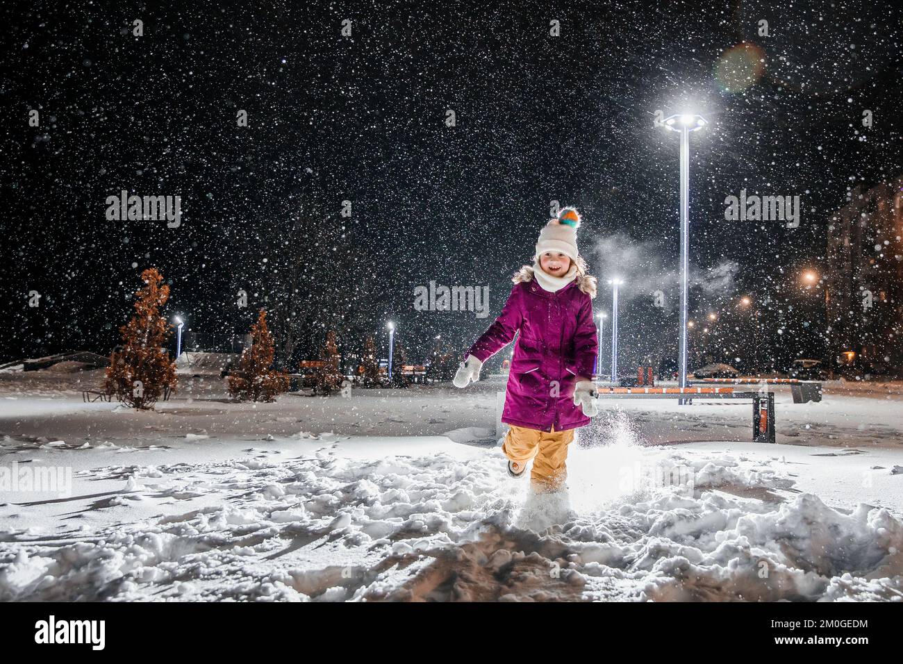 A little girl is very happy with the first snow on a cold winter night. Falling realistic natural snowflakes on a black backgraund. Stock Photo