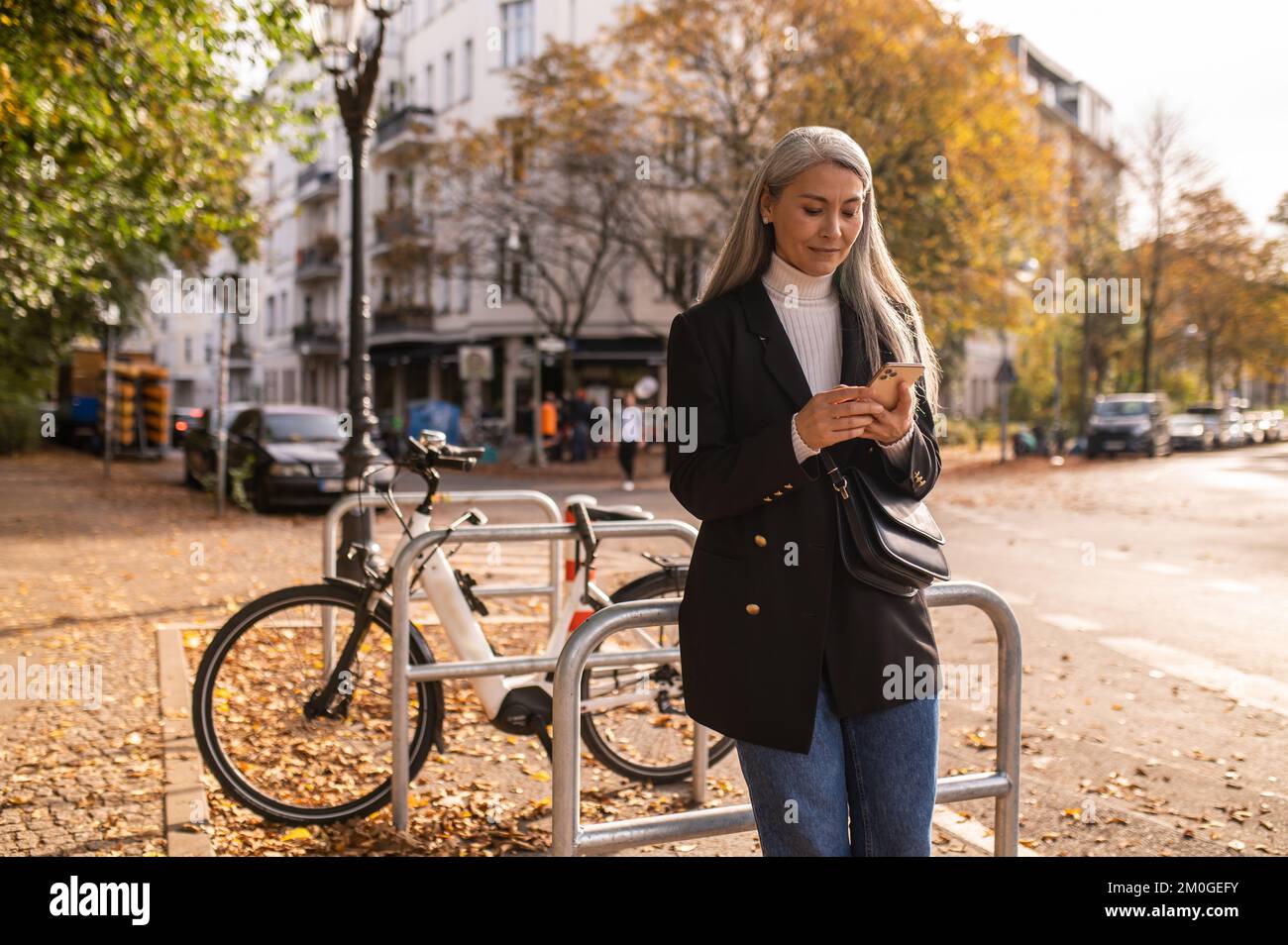 Long-haired mid aged woman with a phone in hand standing near the bikes Stock Photo