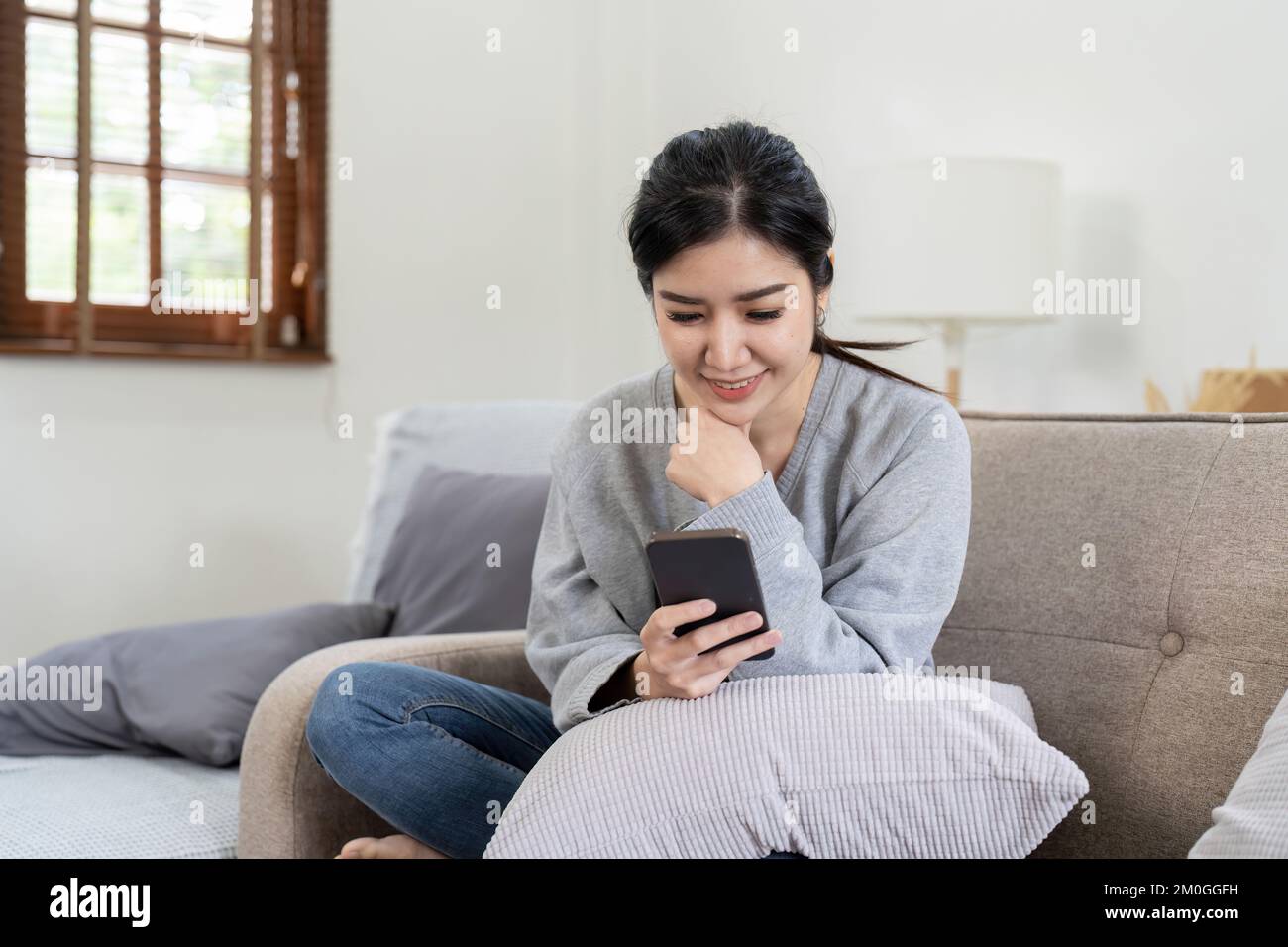 Image of smiling nice asian woman using cellphone while sitting on sofa Stock Photo