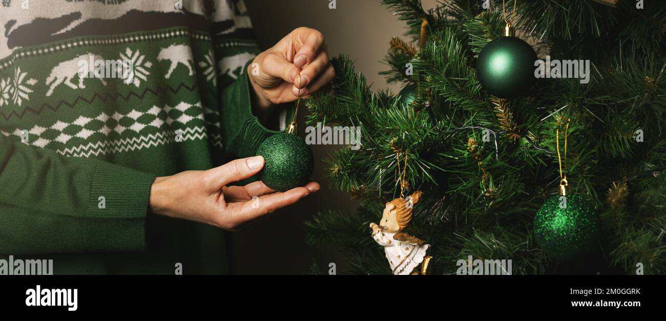 woman decorating a christmas tree at home. hang a green ball on a branch. banner Stock Photo