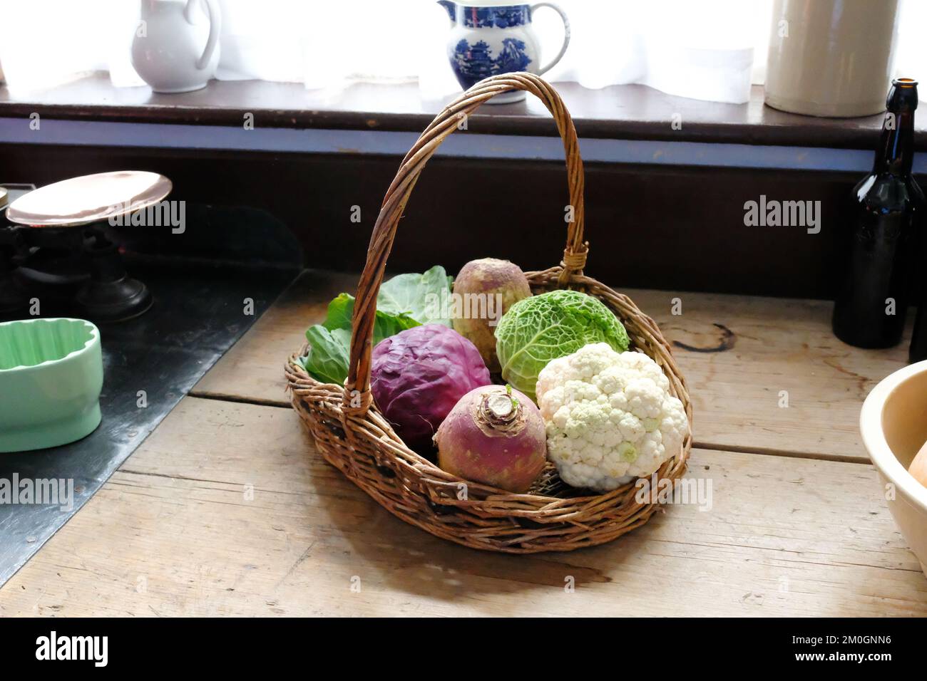 Freshly cut vegetables in a wicker basket on an old fashioned work surface - John Gollop Stock Photo