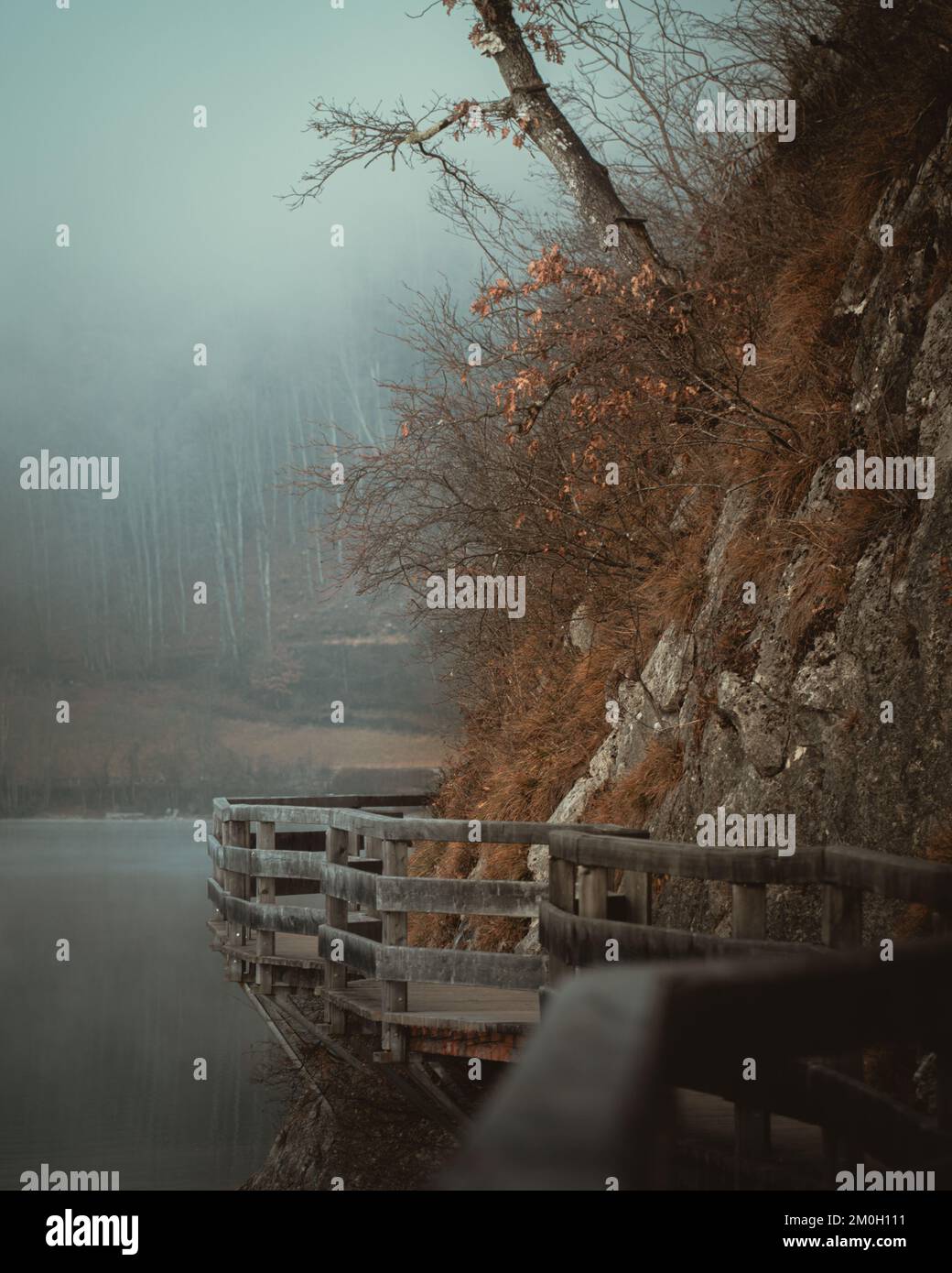 A vertical shot of wooden walkway around rocky hill over lake on foggy ...