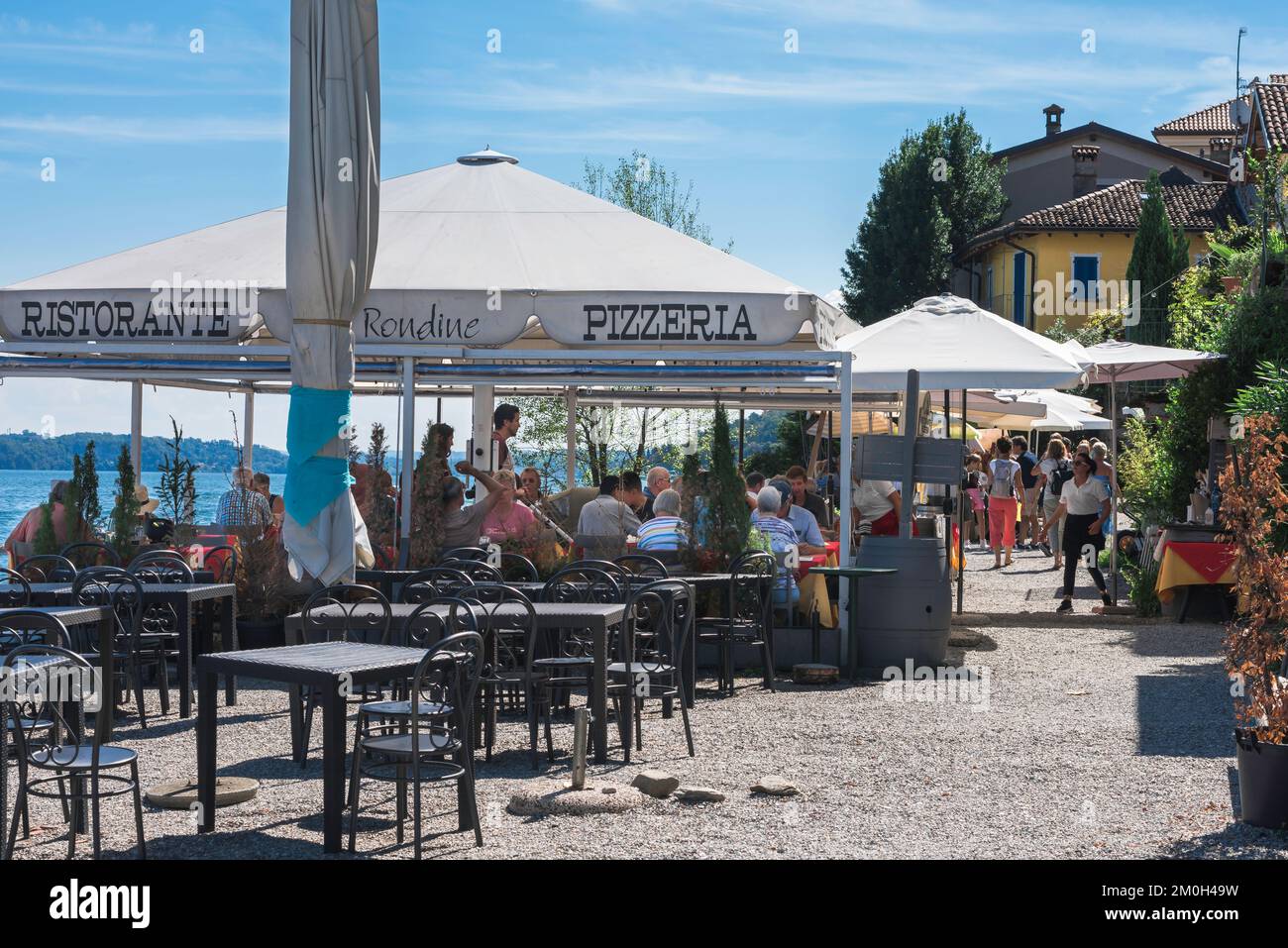 View in summer of people dining at lakeside cafe terraces in the fishing village of Isola dei Pescatori, Borromeo Islands, Lake Maggiore, Italy Stock Photo
