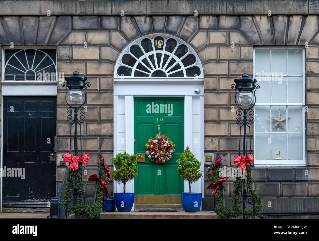 Edinburgh New Town, Scotland, UK, 6th December 2022. Christmas door wreaths: residents in the Georgian townhouses in the New Town are well-known for their splendid decorations. A Georgian front door with fanlight,  Christmas wreath and bows and old fashioned street lamps. Credit: Sally Anderson/Alamy Live News Stock Photo