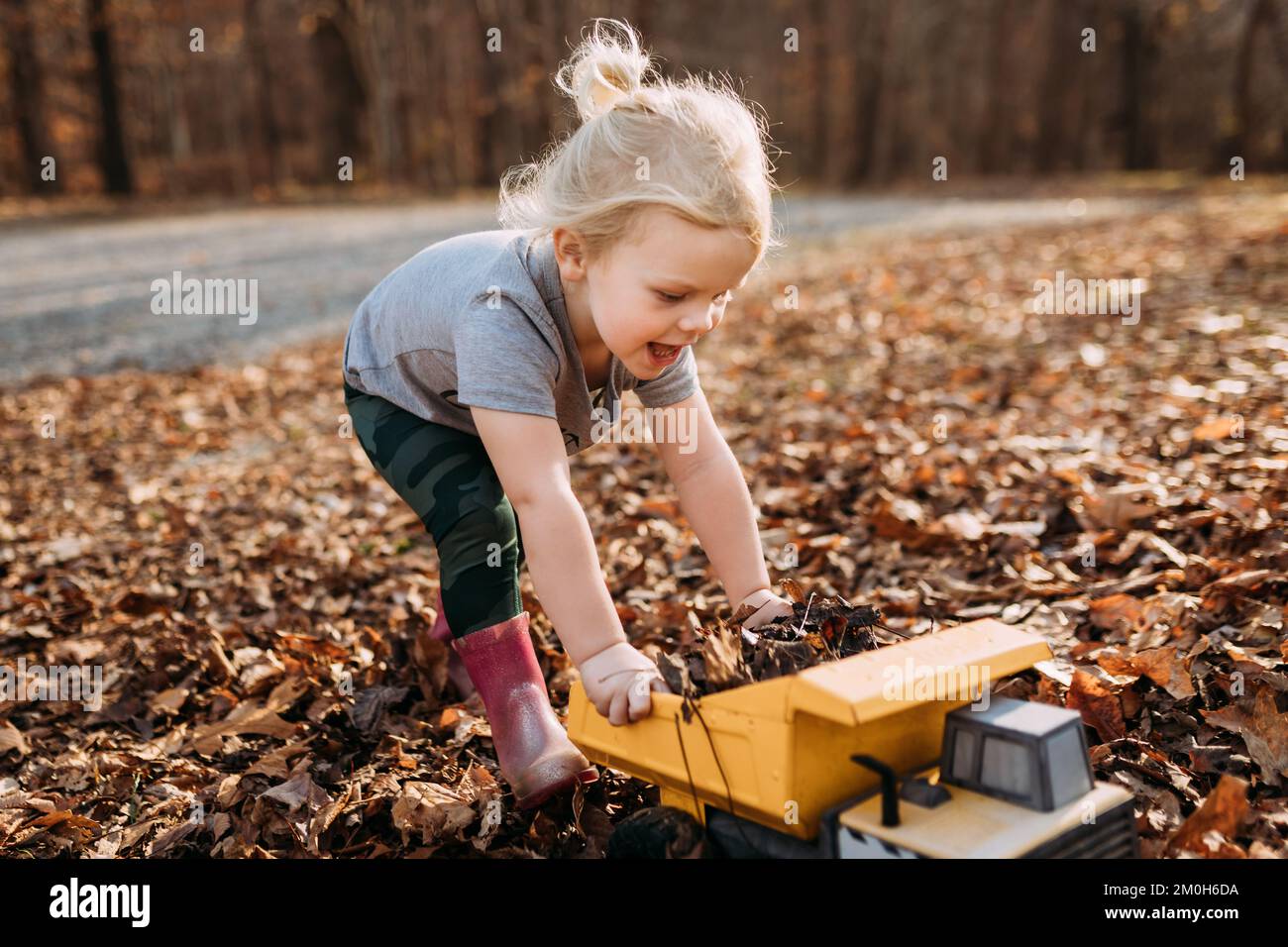 Happy child playing in fall leaves with toy truck Stock Photo - Alamy