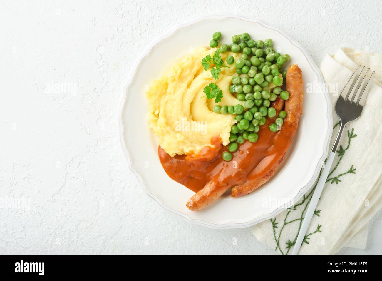 Bangers and mash. Grilled sausages with mash potato and green pea on white plate on light background. Traditional dish of Great Britain and Ireland. B Stock Photo