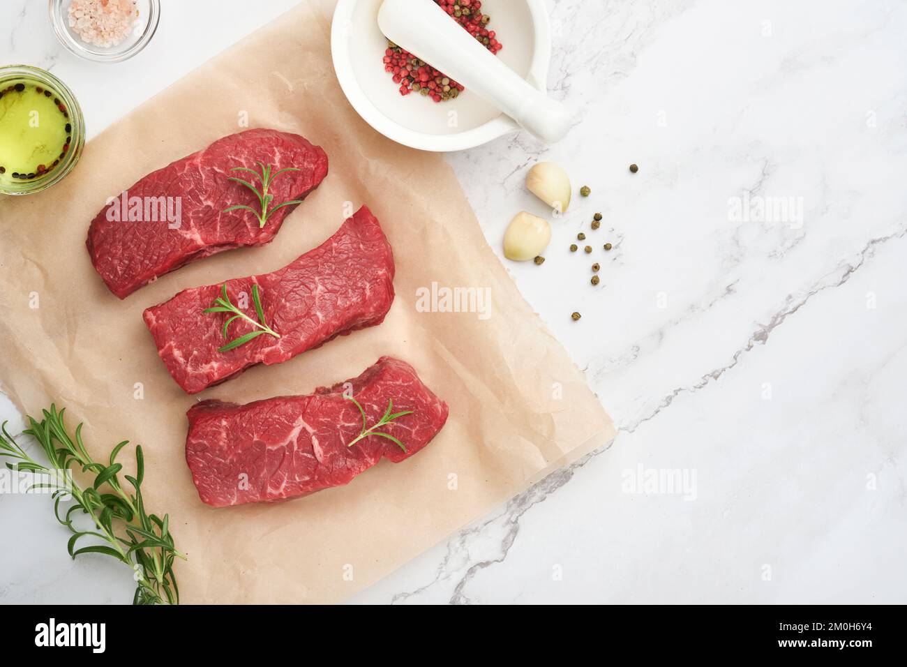 Raw steaks. Top blade steaks on wood burning board with spices, rosemary, vegetables and ingredients for cooking on parchment paper on white backgroun Stock Photo