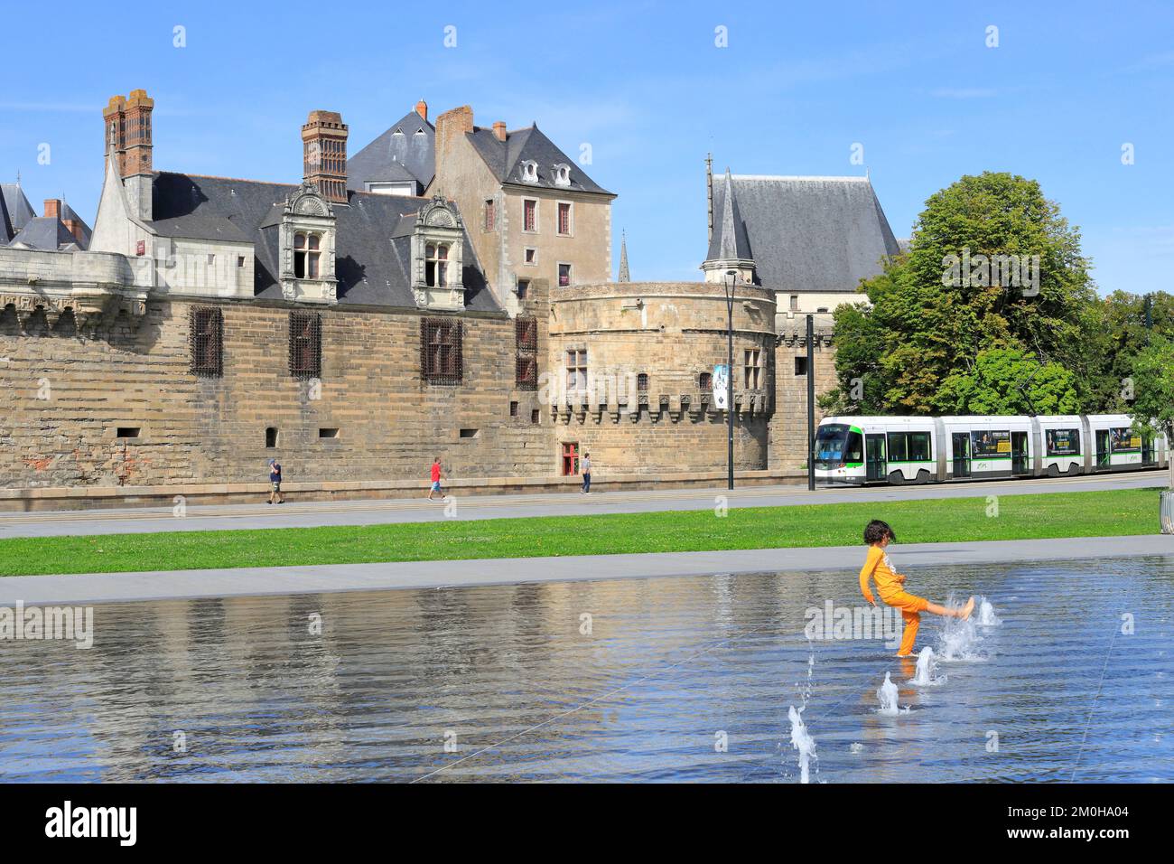 France, Loire Atlantique, Nantes, Elisa Mercoeur square, child playing with the water mirror designed by the architect Bruno Fortier with the tramway and the castle of the Dukes of Brittany in the background Stock Photo