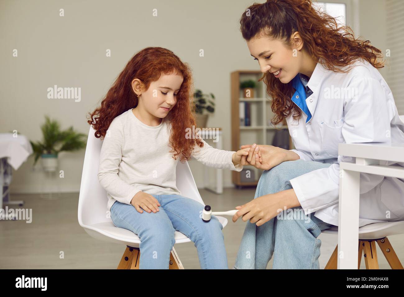 Pediatric neurologist examining happy little child and using hammer to