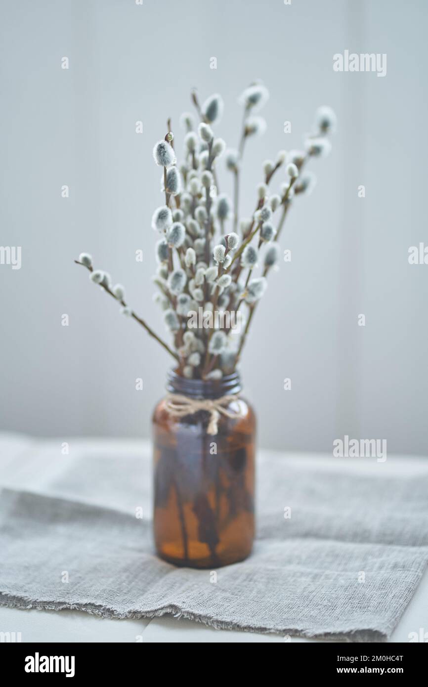A bouquet of willow branches in a brown glass vase stands on the table on a gray napkin. As an interior decoration for Palm Sunday. High quality photo Stock Photo