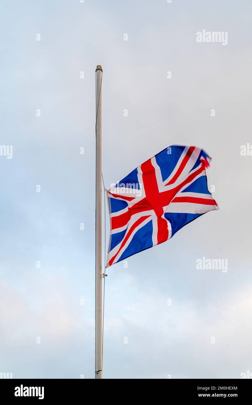 Union Jack flag flying at half mast against a dull pale blue and white