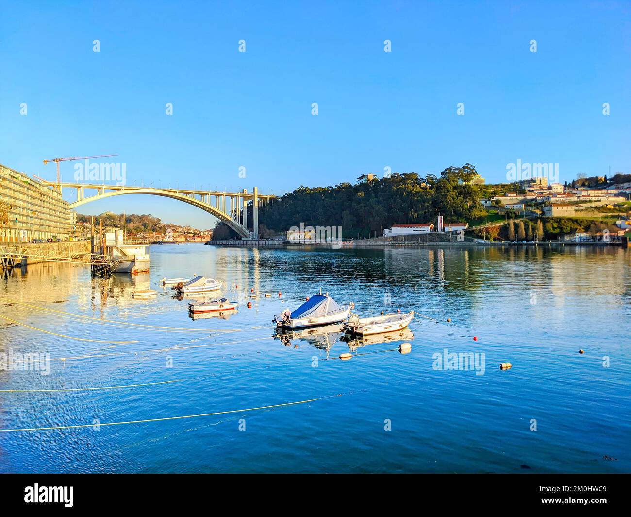Arrabida bridge and fishermen boats moored by embankment in evening sunshine, Porto, Portugal Stock Photo