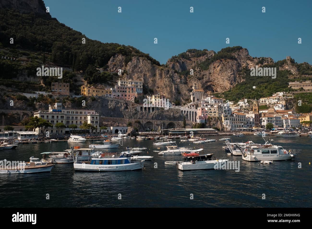 A general view of Amalfi town from the marina wall across to the port and main town with boats in the foreground and limestone cliffs in the background. Stock Photo