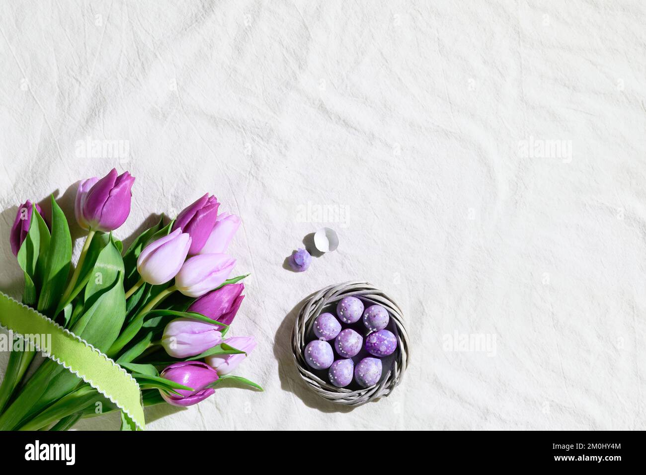 Easter corner composition with bunch of pink magenta tulips and nest, wreath with quail Easter eggs. Flat lay on off white textile tablecloth Stock Photo