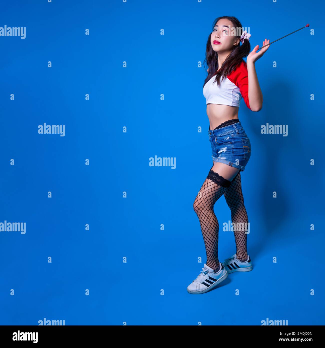 Young Woman in Harlequin Costume Holding Fencing Foil Against a Solid Blue Backdrop Stock Photo