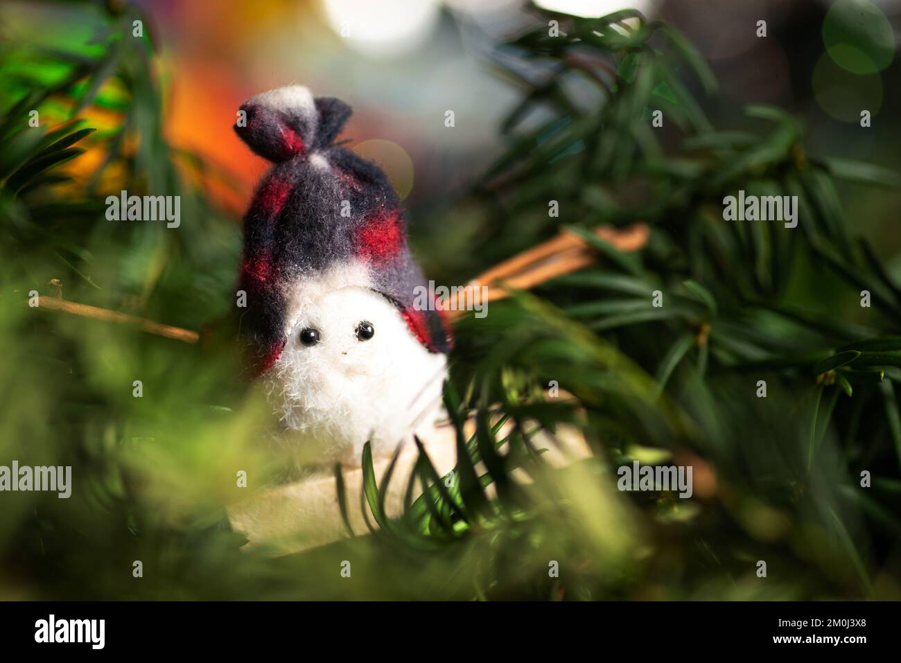 Toy snowman with festive winter holiday decoration and the Christmas tree with shiny fairy lights in the background Stock Photo