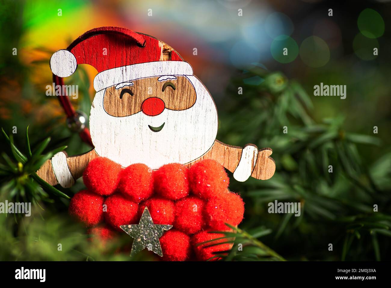 Santa Claus toy and festive winter holiday decoration and the Christmas tree with shiny fairy lights in the background Stock Photo