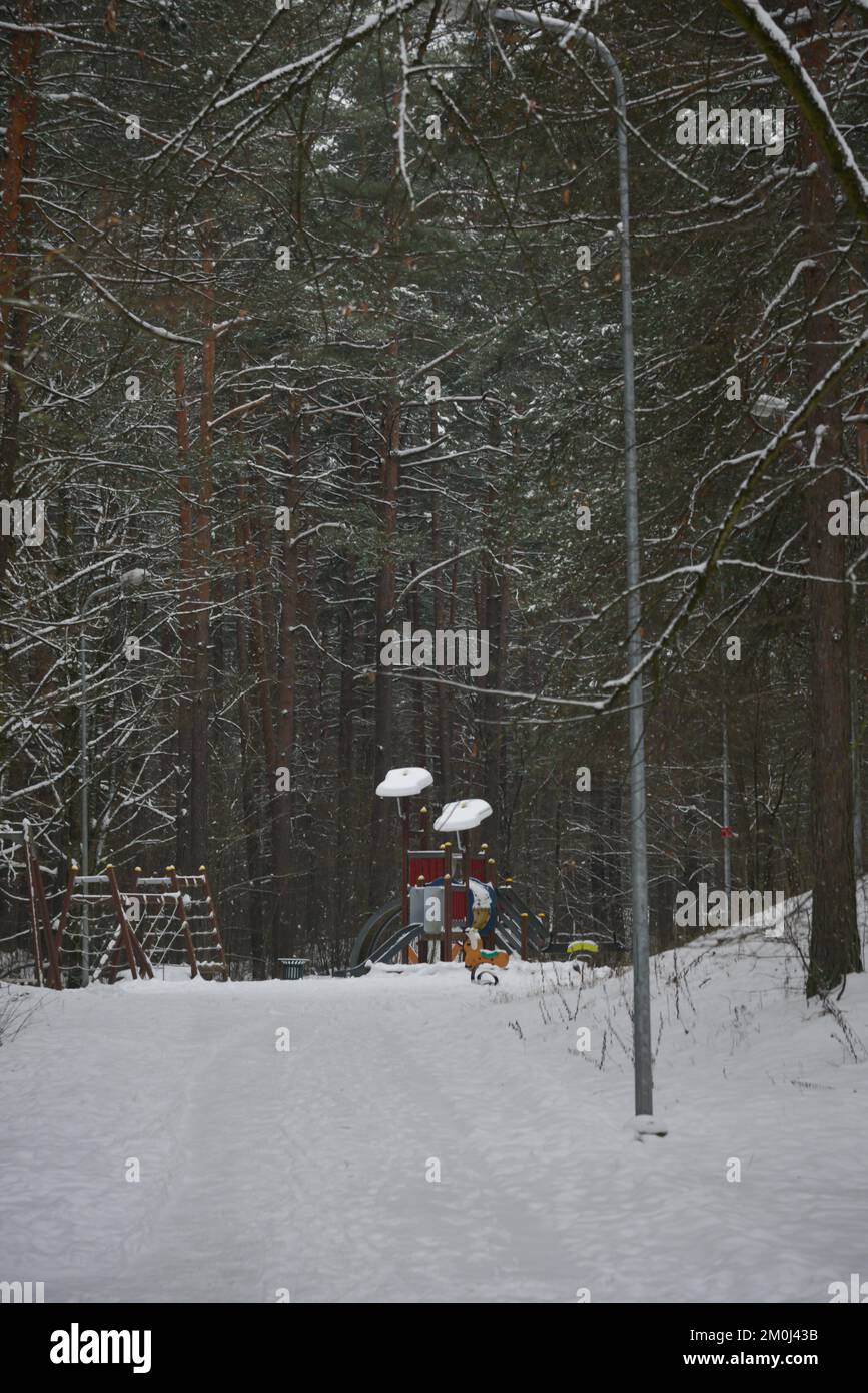 Wooden constructions of the children's playground in the park, to which a snow-covered walking path leads. Stock Photo