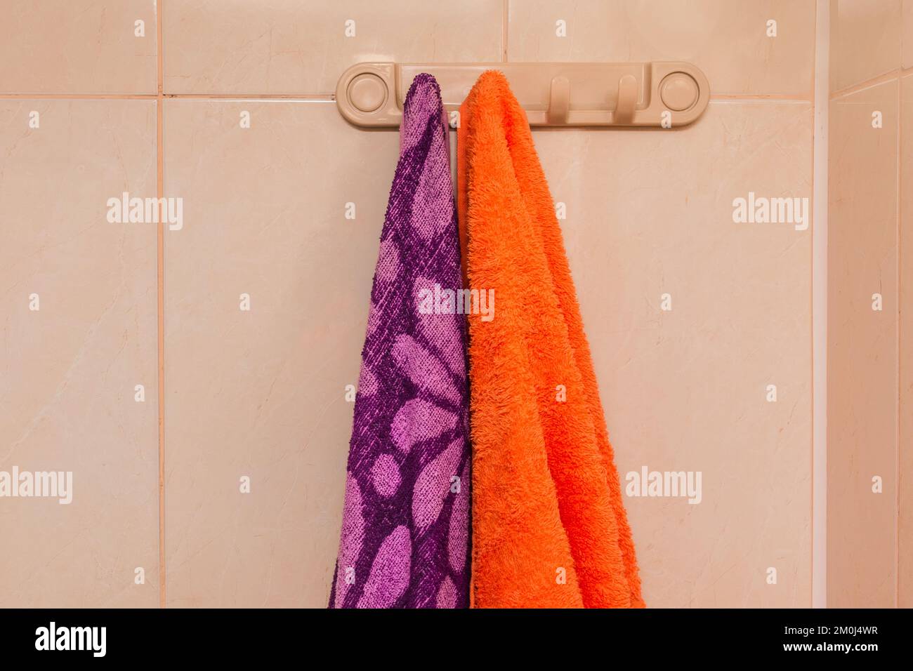 Orange and purple towels hanging on a hanger with hooks in the bathroom