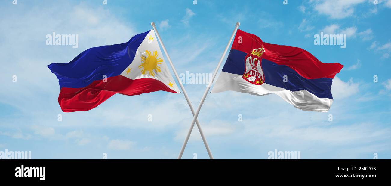 two crossed flags Serbia and Philippines waving in wind at cloudy sky ...