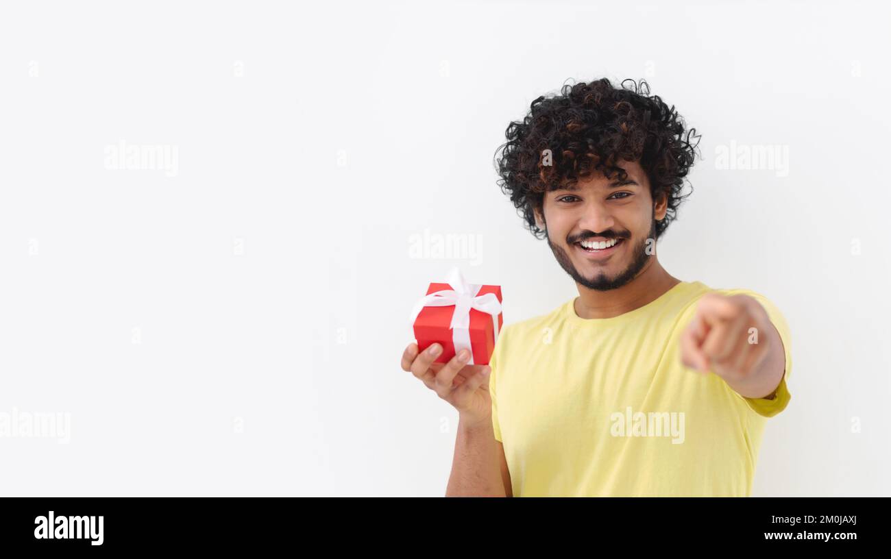 Happy young Asian man with curly hair hold red gift box toothy smile looking at camera on white background Stock Photo
