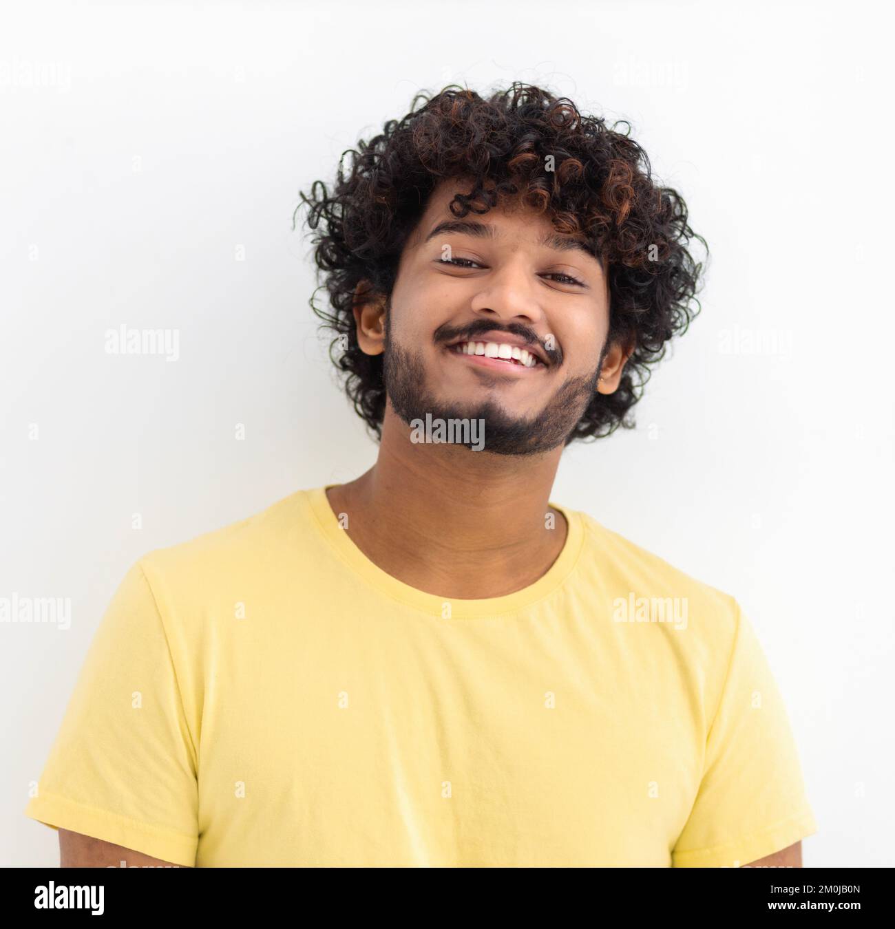 man with curly hair and happy smile. Young Indian male student smiling joyfully standing on a white background Stock Photo