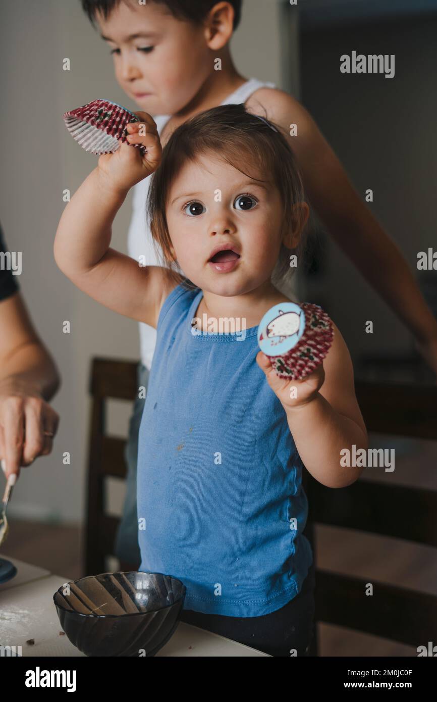 Mother teaching small adorable kid preparing dough for homemade pastry, cooking together in modern kitchen. Family cooking muffins together. Adorable Stock Photo