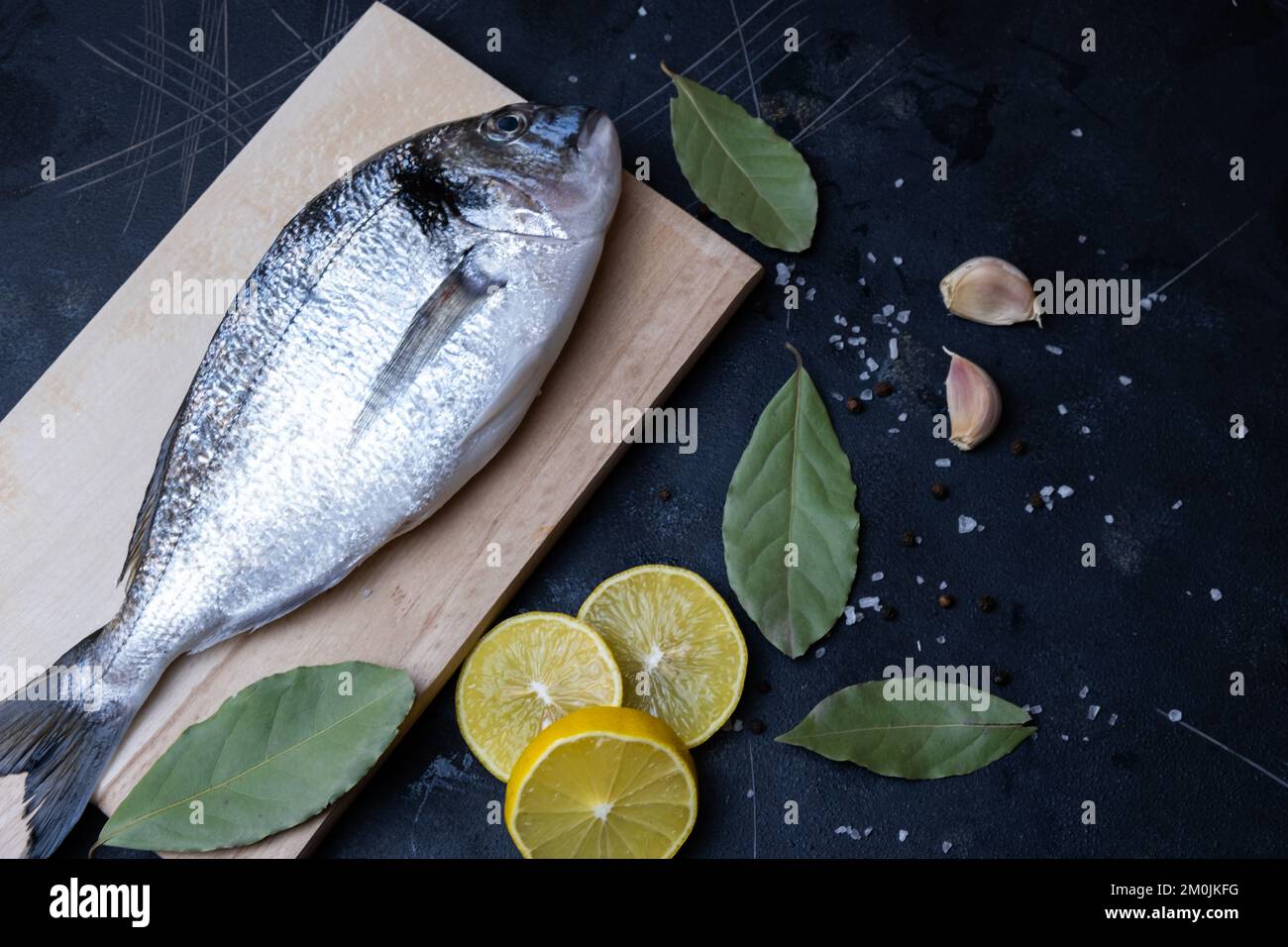 Ready to cook raw sea bream or dorada sea fish. Top view of lemon, garlic on dark background