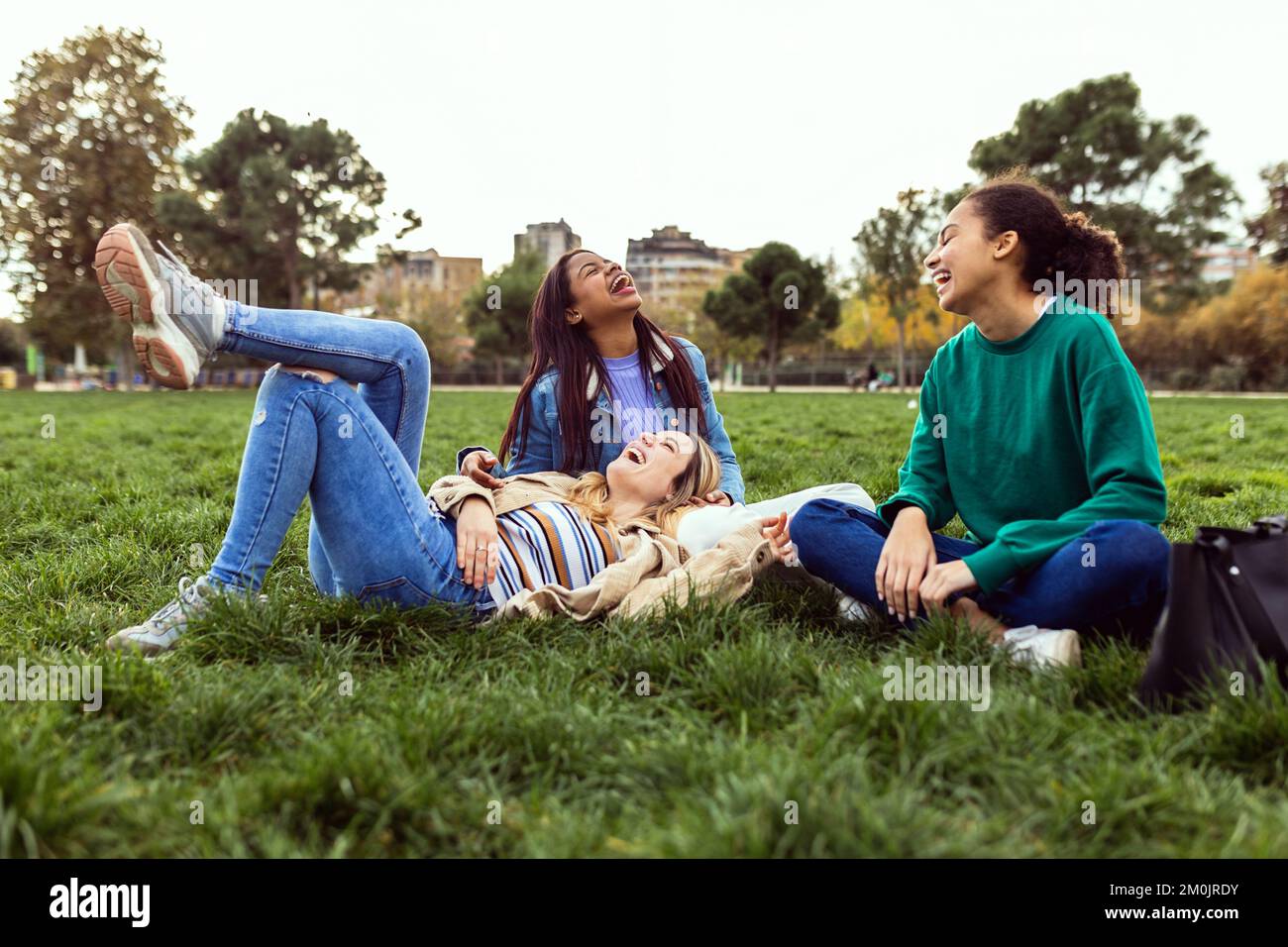 Three happy young women having fun sitting on green grass at park Stock Photo