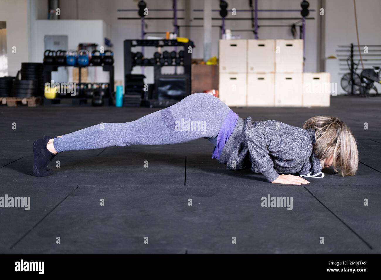 A blond mid adult woman practicing vinyasa flow yoga alone in a gym, wearing sportswear and doing a plank. Stock Photo