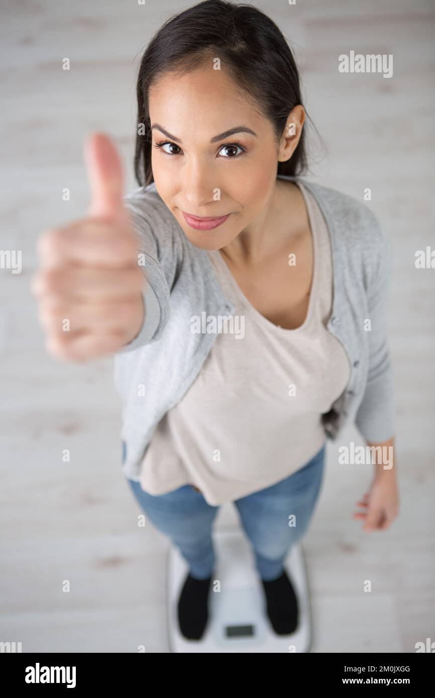 woman stading on bathroom scales holding thumbs up Stock Photo Alamy