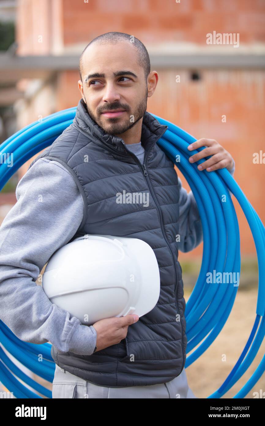 builder carrying reel of blue pipe on his shoulder Stock Photo