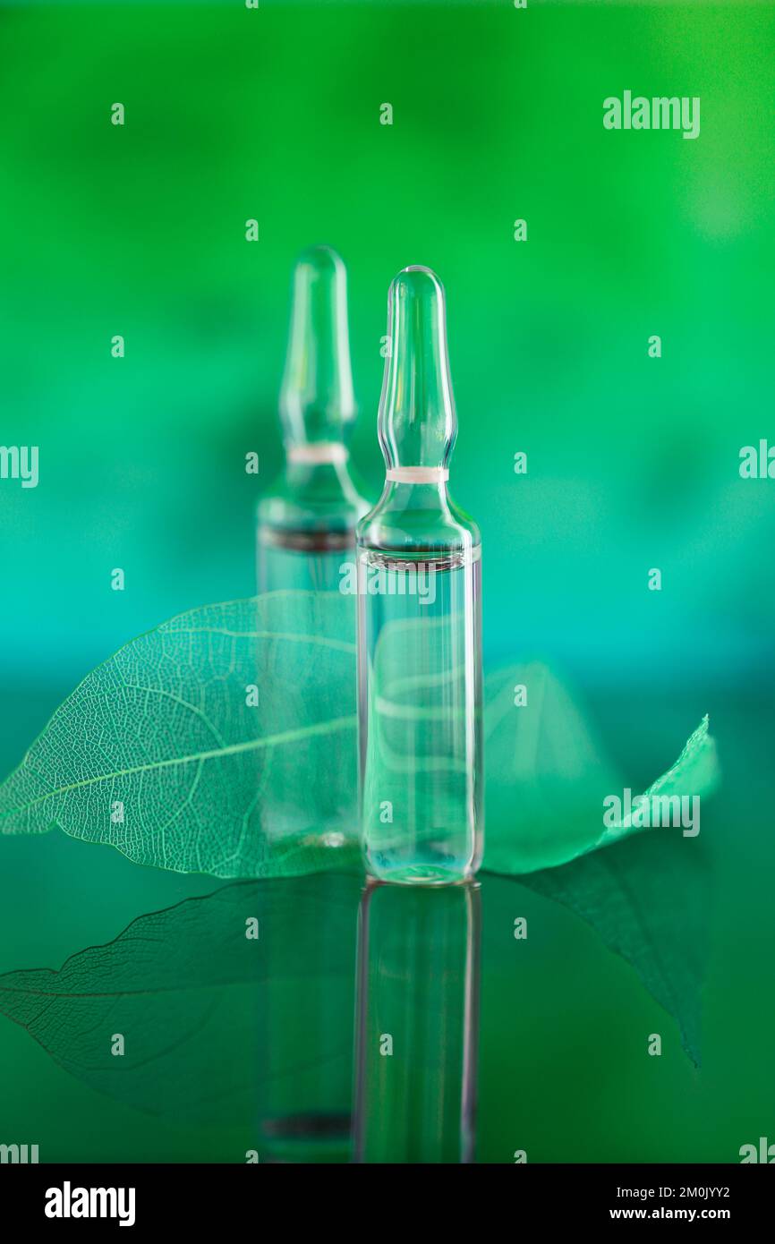 cosmetic ampoules and green skeletonized leaves on a turquoise green blurred background.Mesotherapy and dermabrasion serum in ampoules.Hyaluronic acid Stock Photo