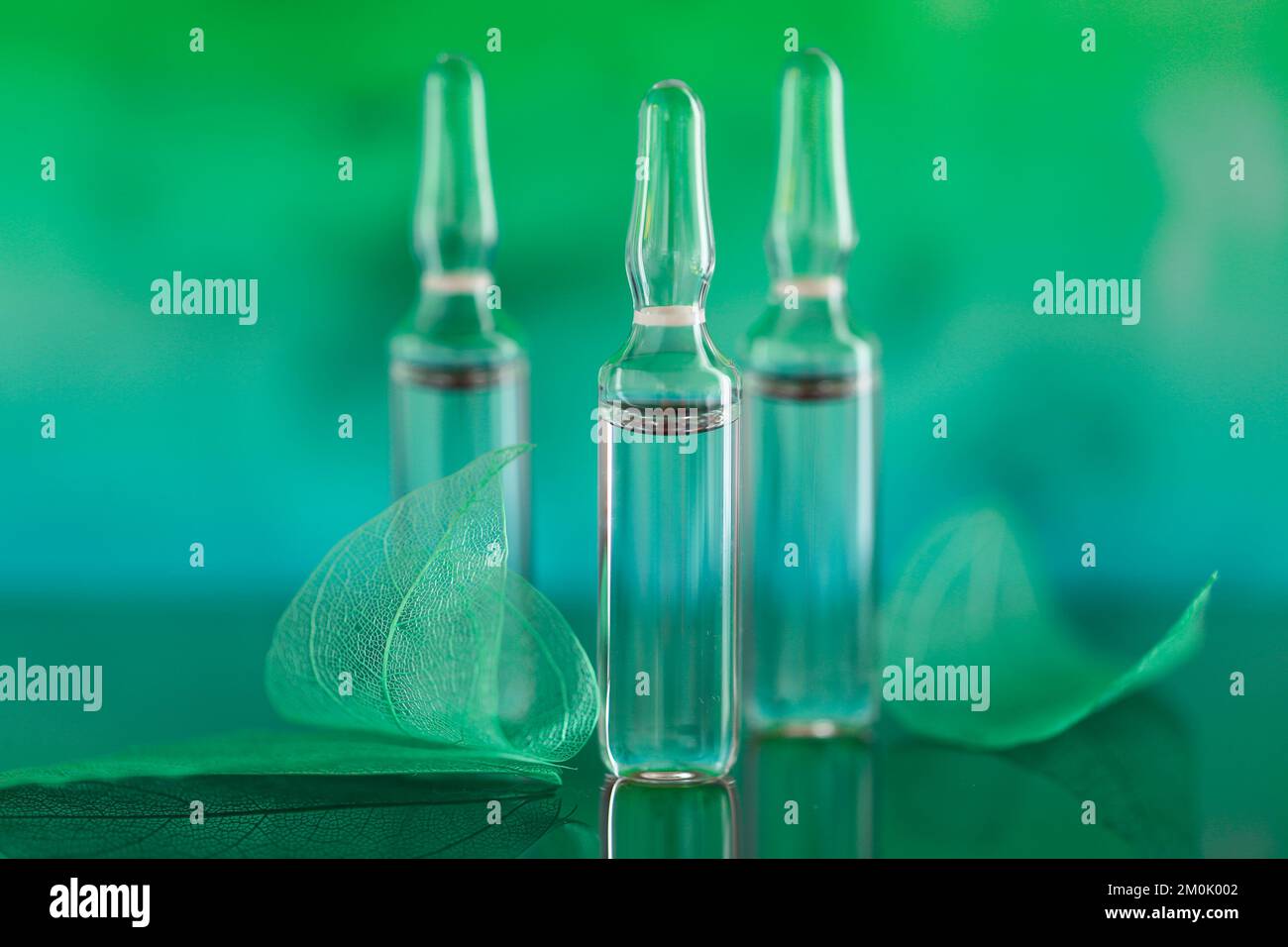 ampoules and green skeletonized leaves on a turquoise blurred background.Mesotherapy and dermabrasion serum in ampoules.Hyaluronic acid in ampoules. Stock Photo
