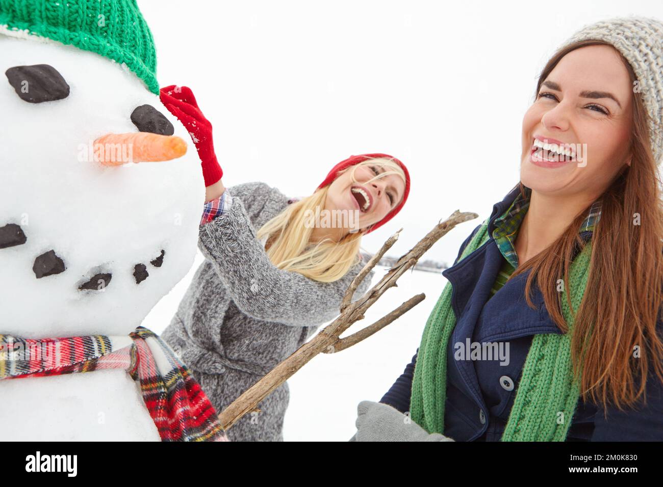 Friends, snowman and women building in the snow on a cold winter day in the UK while having fun. Playing, playful female friendship while creating a Stock Photo