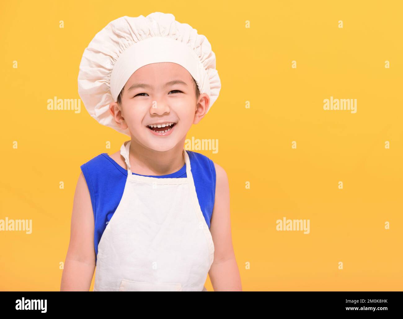 Happy kid in chef uniform  on yellow background Stock Photo