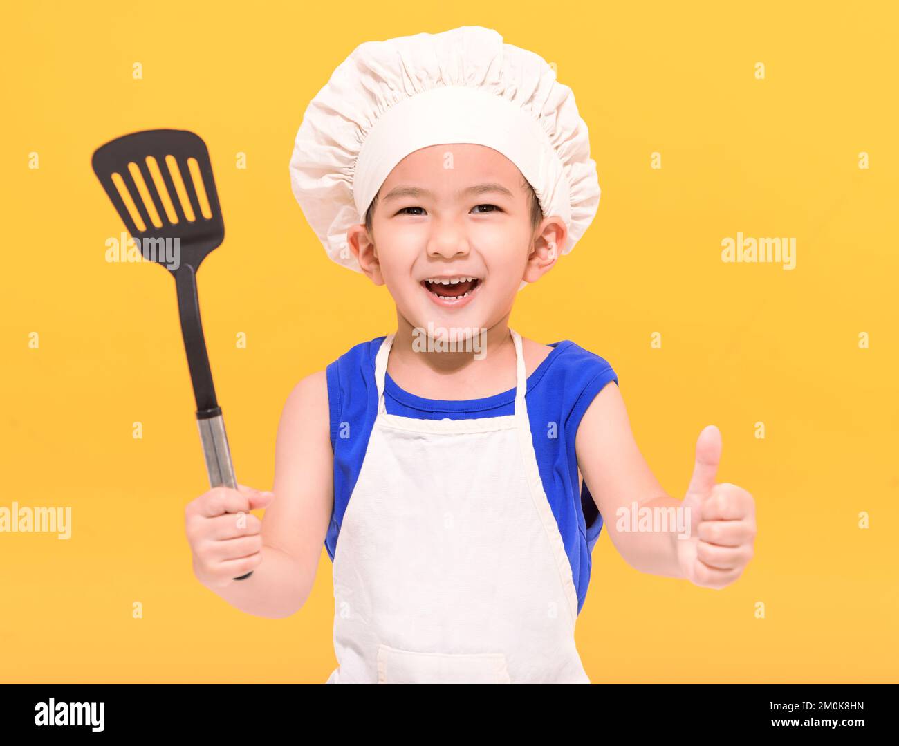 Happy little boy in chef uniform showing thumbs up  on yellow background Stock Photo