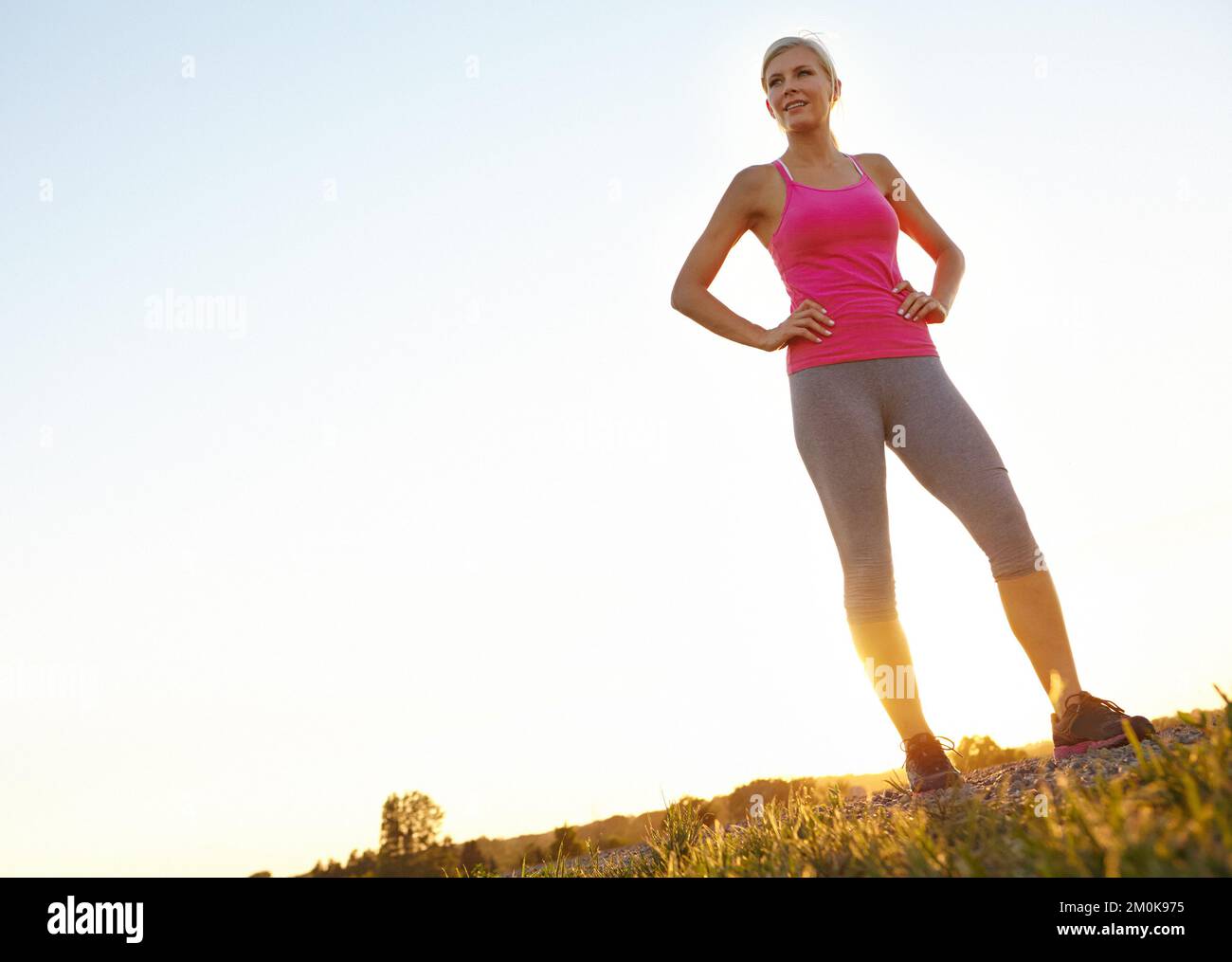 Building confidence with fitness. A young woman standing with arms akimbo in a field wearing sportswear. Stock Photo