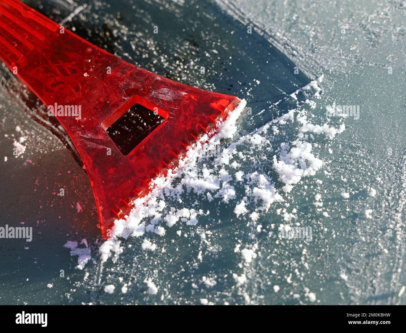 red scraper removes ice from the car windshield, close up Stock Photo