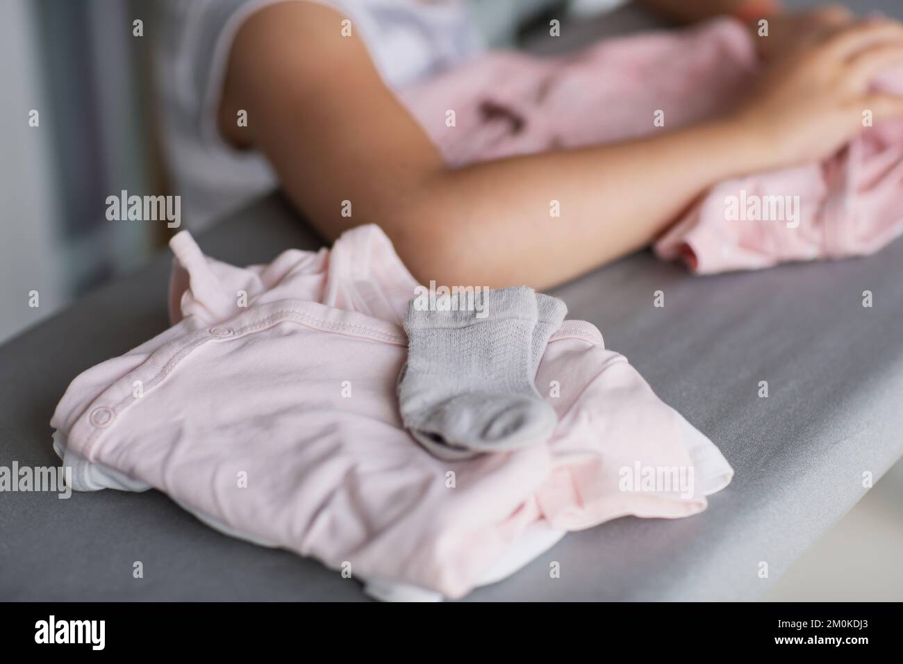 Cute little girl is leaning on ironing clothes on board at home