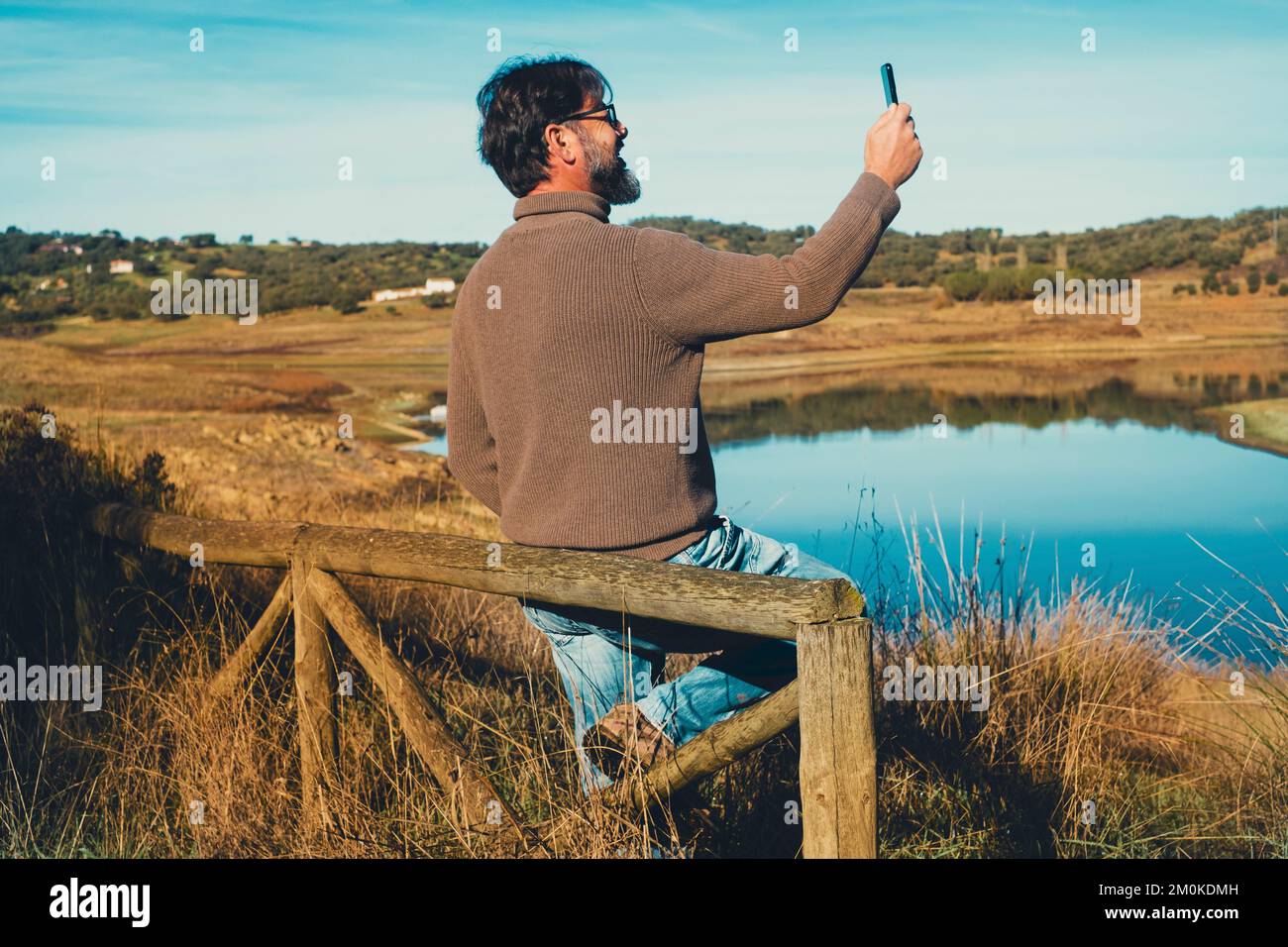 One male tourist take landscape picture using mobile phone with lake view. One man enjoying outdoor leisure activity at the park and stay connected wi Stock Photo