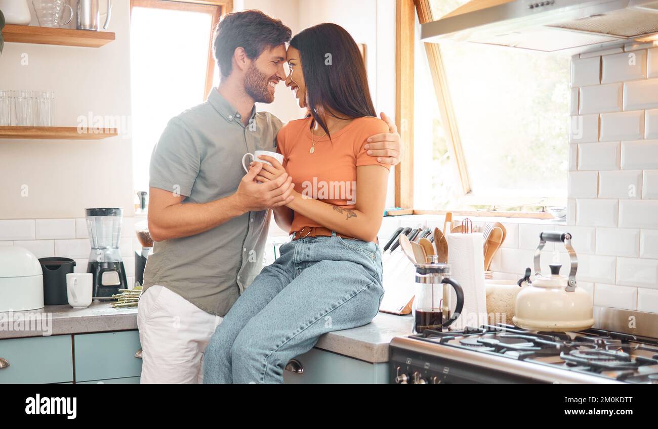 Young happy interracial couple bonding while drinking tea together at home. Loving caucasian boyfriend and mixed race girlfriend standing in the Stock Photo