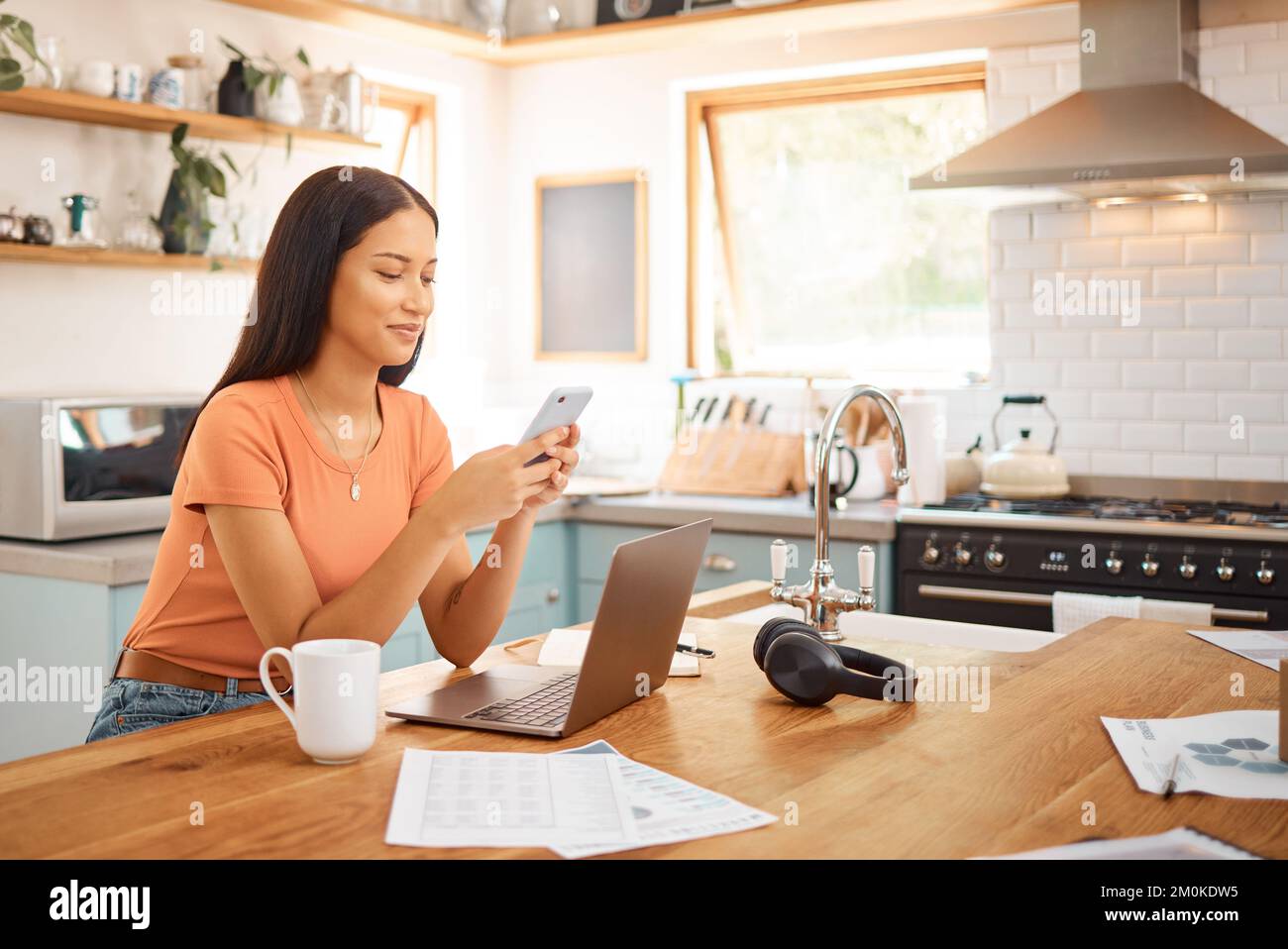 Young happy mixed race businesswoman using a phone while working from home. One content hispanic woman using social media on her cellphone while using Stock Photo